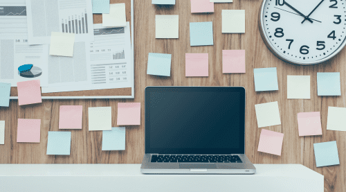 Bureau encombré de post-it colorés, graphique d’objectifs et ordinateur portable fermé, représentant le trop-plein de tâches à gérer.
